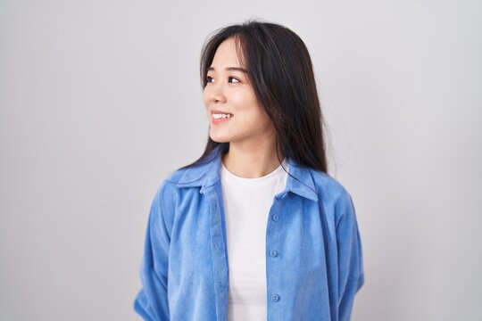Young chinese woman standing over white background looking away to side with smile on face, natural expression. laughing confident.