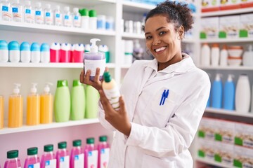African american woman pharmacist smiling confident holding gel bottles at pharmacy