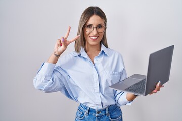 Young woman working using computer laptop smiling with happy face winking at the camera doing victory sign with fingers. number two. - obrazy, fototapety, plakaty