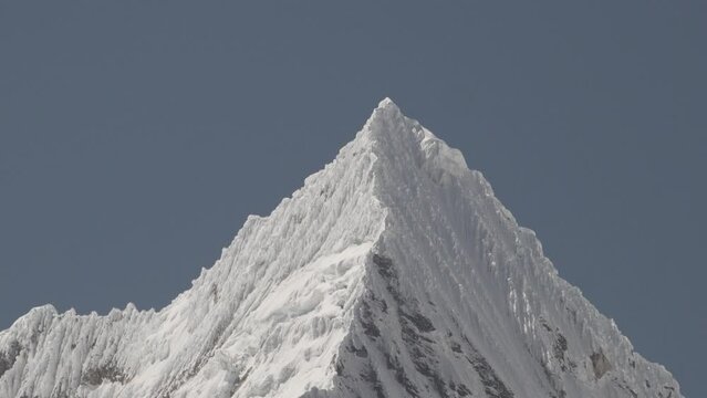 ice covered glacier of a pyramid shaped mountain at laguna paron lagoon in the high andes mountains of the cordillera blanca at huascaran, Peru, with snow covered mountain peaks on a bright sunny day.