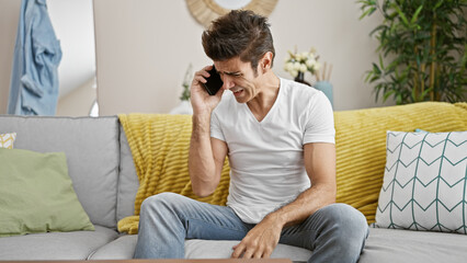 Young hispanic man speaking on the phone angry arguing at home