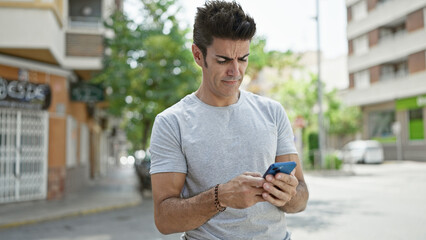 Young hispanic man using smartphone with serious expression at street