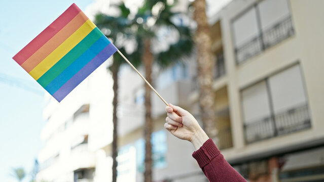 Young hispanic man holding rainbow flag at street