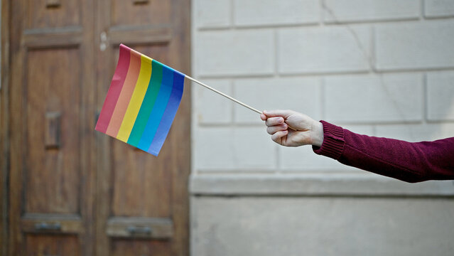 Young hispanic man holding rainbow flag at street