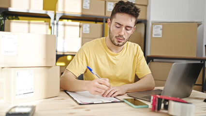 Obraz premium Young hispanic man ecommerce business worker checking packages writing on clipboard at office