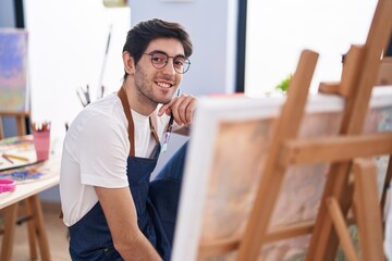Young hispanic man artist smiling confident looking draw at art studio
