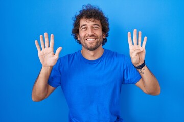 Hispanic young man standing over blue background showing and pointing up with fingers number nine while smiling confident and happy.