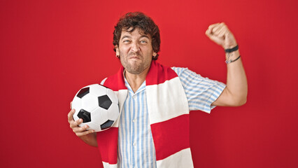 Young hispanic man supporting soccer team celebrating over isolated red background