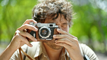 Young hispanic man tourist wearing backpack taking pictures with vintage camera at park