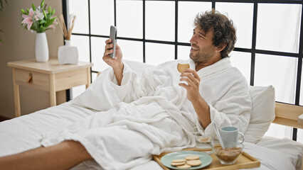 Young hispanic man having breakfast doing video call at bedroom