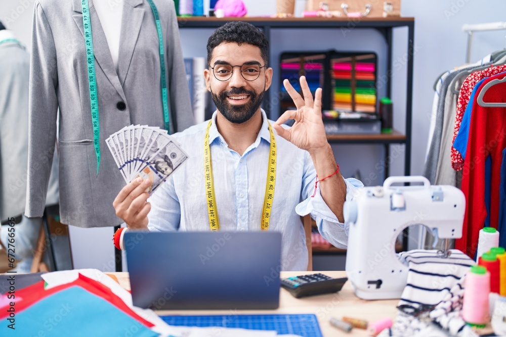 Poster Hispanic man with beard dressmaker designer holding dollars doing ok sign with fingers, smiling friendly gesturing excellent symbol