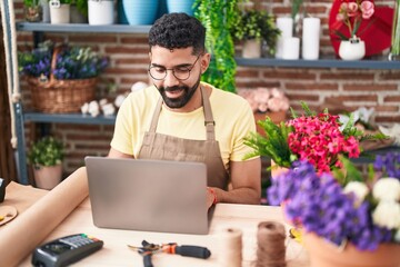 Young arab man florist smiling confident using laptop at florist