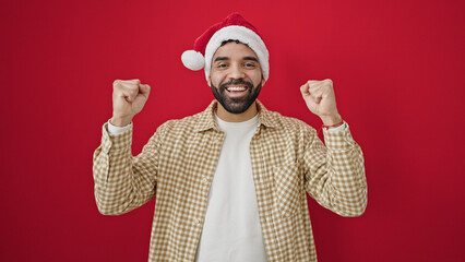 Fototapeta na wymiar Young hispanic man wearing christmas hat with winner expression over isolated red background
