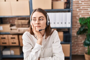 Young caucasian woman working at small business ecommerce wearing headset thinking looking tired...