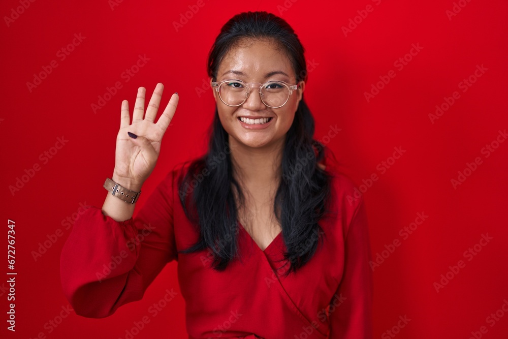 Sticker Asian young woman standing over red background showing and pointing up with fingers number four while smiling confident and happy.