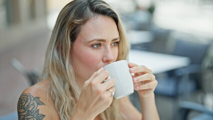 Young blonde woman drinking coffee sitting on table at coffee shop terrace