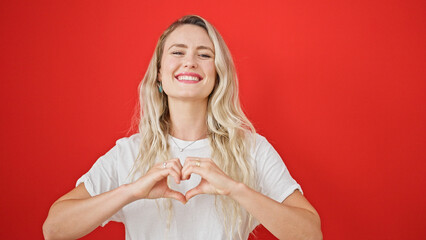 Young blonde woman smiling confident doing heart gesture with hands over isolated red background - obrazy, fototapety, plakaty