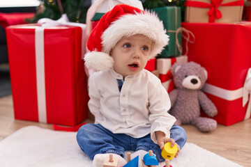Fototapeta na wymiar Adorable blond toddler playing with wooden train sitting on floor by christmas gifts at home