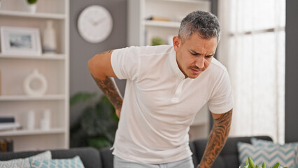 Young hispanic man suffering for backache standing at home