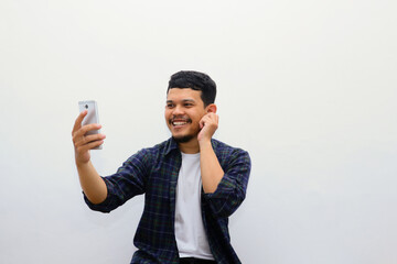Portrait of happy 20s aged Asian man in casual clothing making facetime video calling with smartphone at home. He's waving at people on phone screen. Social distancing concept