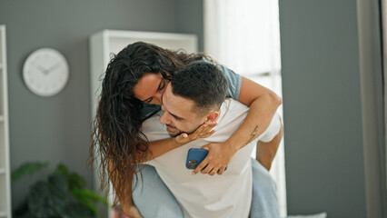 Man and woman couple holding smartphone holding girlfriend on back at home