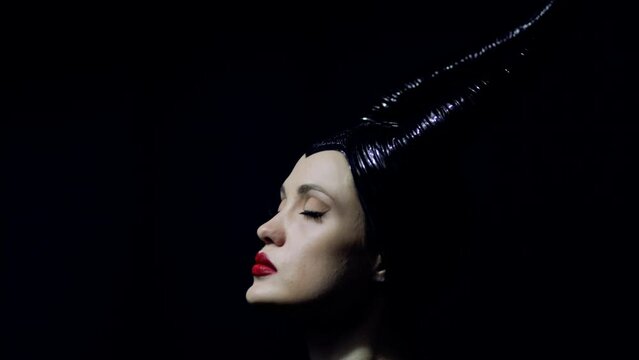  beautiful woman with devil witch horns in sorceress costume. Woman in Halloween costume posing against black background.
