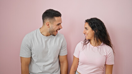 Man and woman couple standing together looking each other over isolated pink background