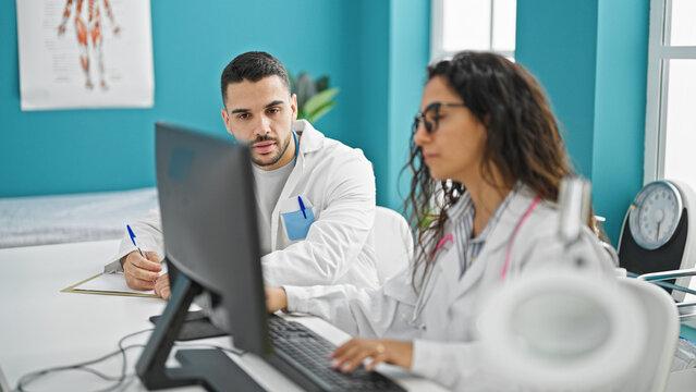 Man and woman doctors using computer taking notes speaking at the clinic