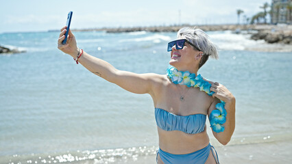 Young woman tourist wearing bikini and hawaiian lei having video call at beach