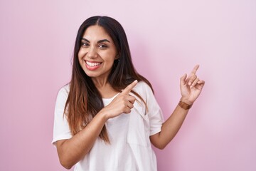 Young arab woman standing over pink background smiling and looking at the camera pointing with two...