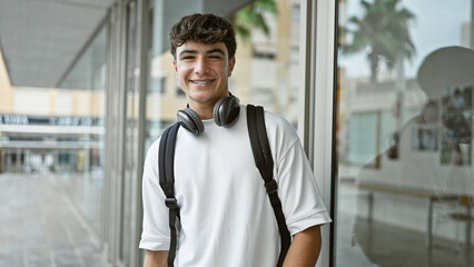 Cheerful young hispanic male student standing outdoors enjoying campus life, confidently wearing...