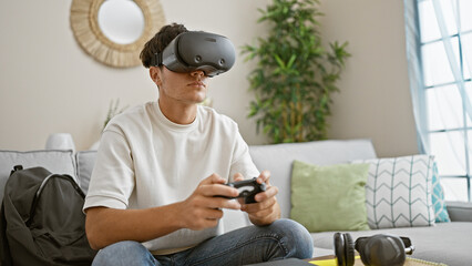 Engrossed young hispanic teenager immerses in gaming universe at home, using virtual reality glasses and joystick, living a relaxed yet concentrated 3d lifestyle