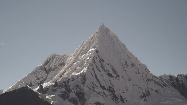 ice covered glacier of a pyramid shaped mountain at laguna paron lagoon in the high andes mountains of the cordillera blanca at huascaran, Peru, with snow covered mountain peaks on a bright sunny day.