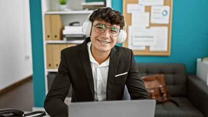 Young hispanic business whiz, a smiling teenager working with laptop and headphones at the office