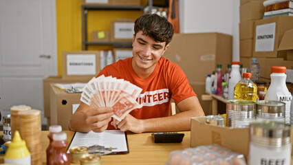 Smiling young hispanic teenager joyfully volunteers at charity center, confidently holding iceland krona banknotes - obrazy, fototapety, plakaty