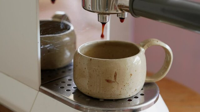 Close up of automatic coffee machine with coffee capsules or coffee pods pouring espresso drink. Coffee steam into beautiful ceramic or clay cup. Close up shot on old machine. 4k high quality.