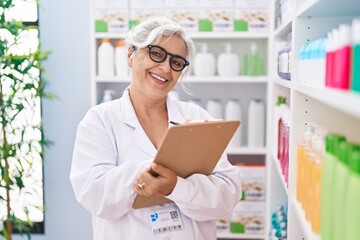 Middle age grey-haired woman pharmacist writing on document at pharmacy