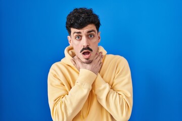 Hispanic man standing over blue background shouting suffocate because painful strangle. health problem. asphyxiate and suicide concept.