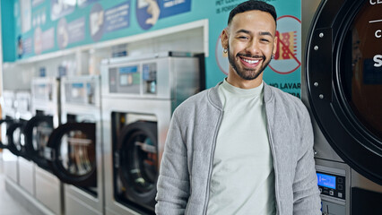 Young hispanic man smiling confident standing at laundry facility