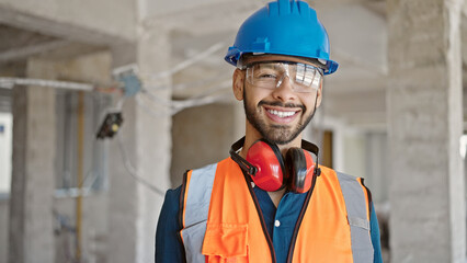 Young hispanic man builder smiling confident wearing hardhat at construction site