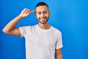 Naklejka premium Young hispanic man standing over blue background smiling pointing to head with one finger, great idea or thought, good memory