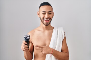 Young hispanic man holding electric razor smiling happy pointing with hand and finger - obrazy, fototapety, plakaty