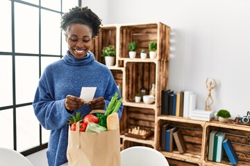 African american woman smiling confident reading food receipt at home - obrazy, fototapety, plakaty