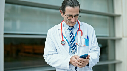 Middle age man doctor smiling confident using smartphone at hospital