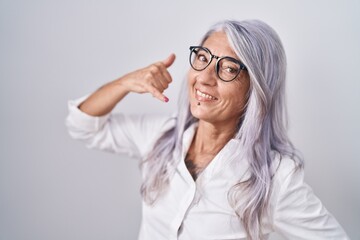 Middle age woman with tattoos wearing glasses standing over white background smiling doing phone gesture with hand and fingers like talking on the telephone. communicating concepts.
