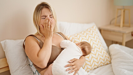 Mother and daughter sitting on bed breastfeeding baby tired yawning at bedroom