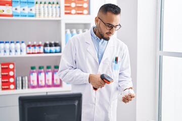 Young hispanic man pharmacist scanning pills bottle at pharmacy