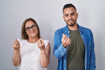Hispanic mother and son standing together doing money gesture with hands, asking for salary payment, millionaire business