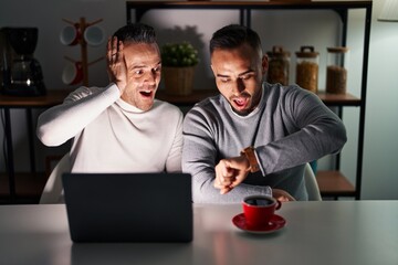 Homosexual couple using computer laptop looking at the watch time worried, afraid of getting late