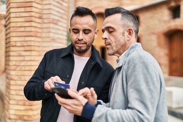 Two men couple using smartphone with relaxed expression at street